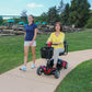 Woman enjoying the outdoors on a Go-Go Sport scooter rental with a companion walking beside her.